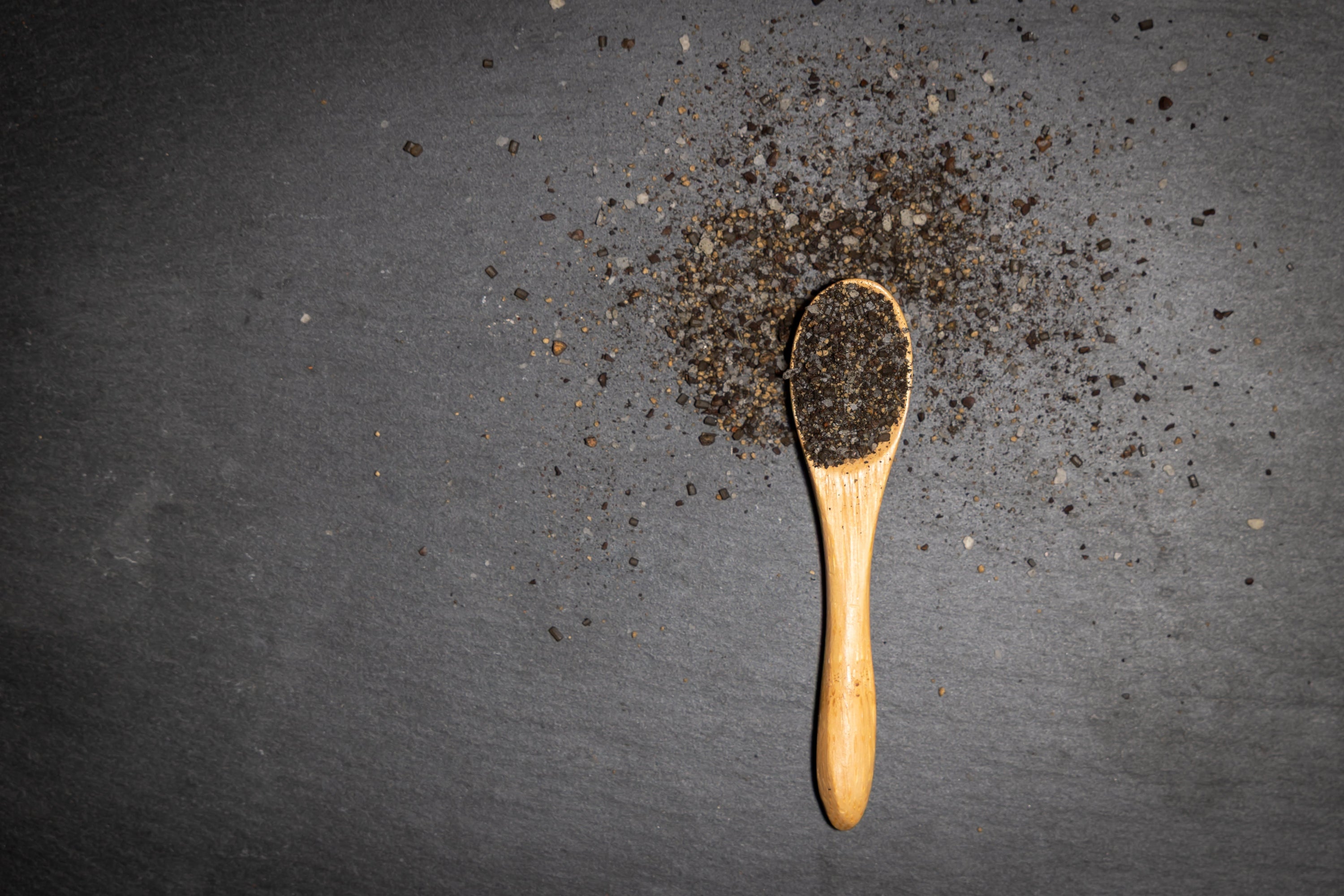 Wooden spoon with black pepper on a dark surface