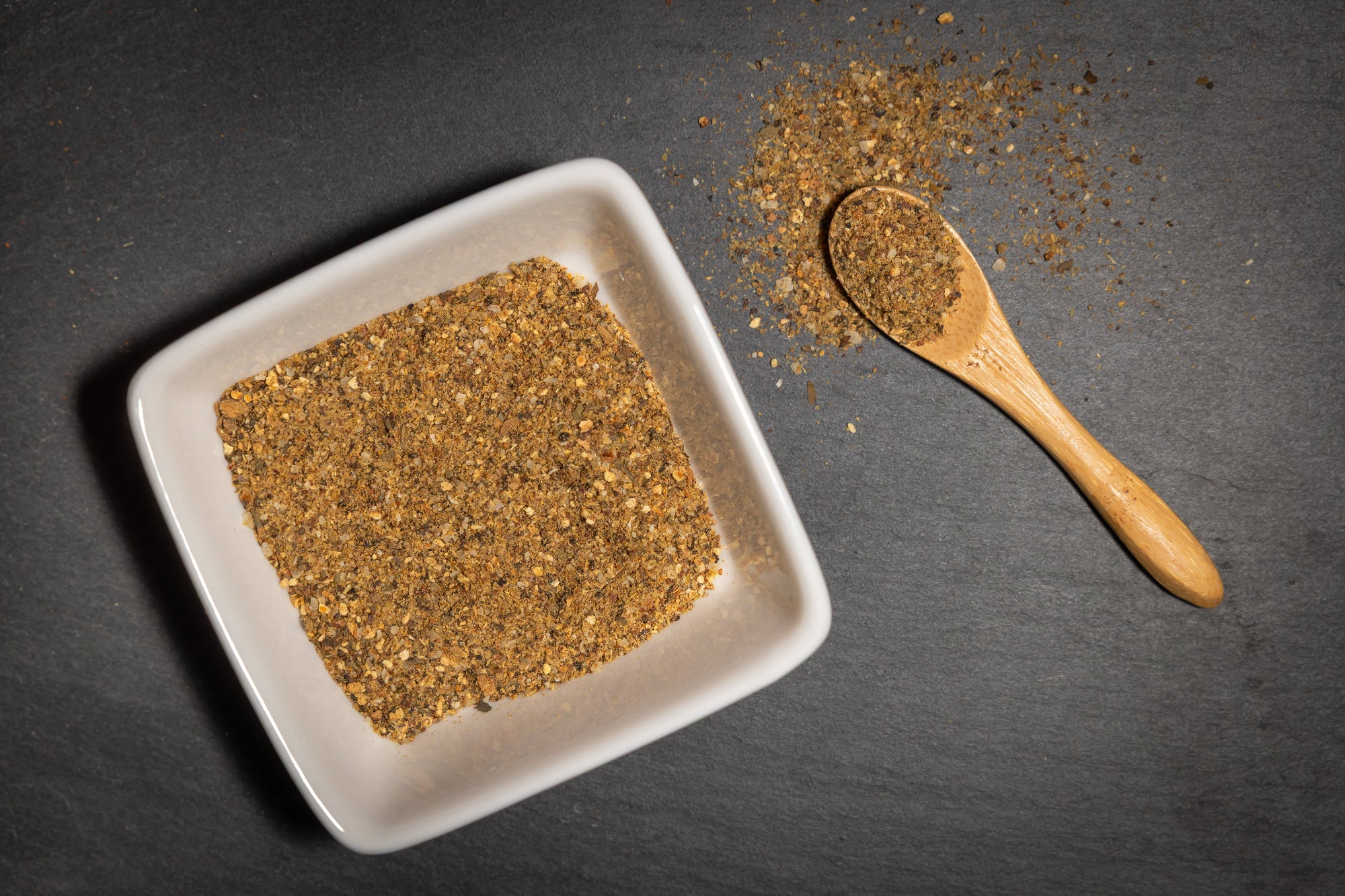 Spice mix on a white plate with a wooden spoon on a dark surface