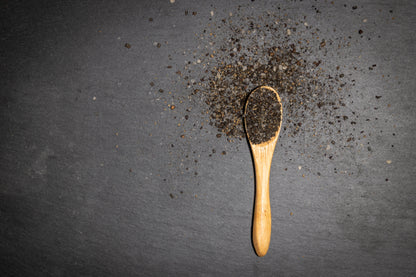 Wooden spoon with black pepper on a dark surface